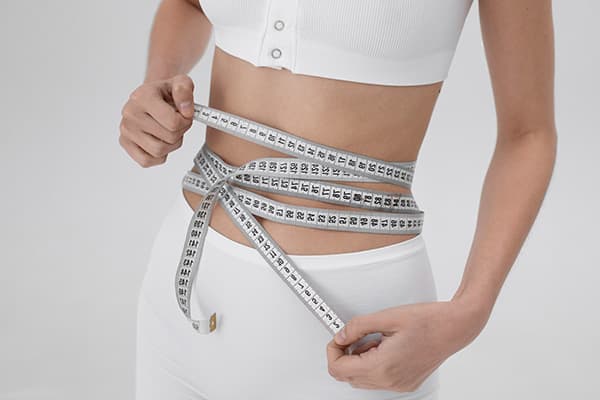 A person attempting to track their weight loss with a measuring tape
